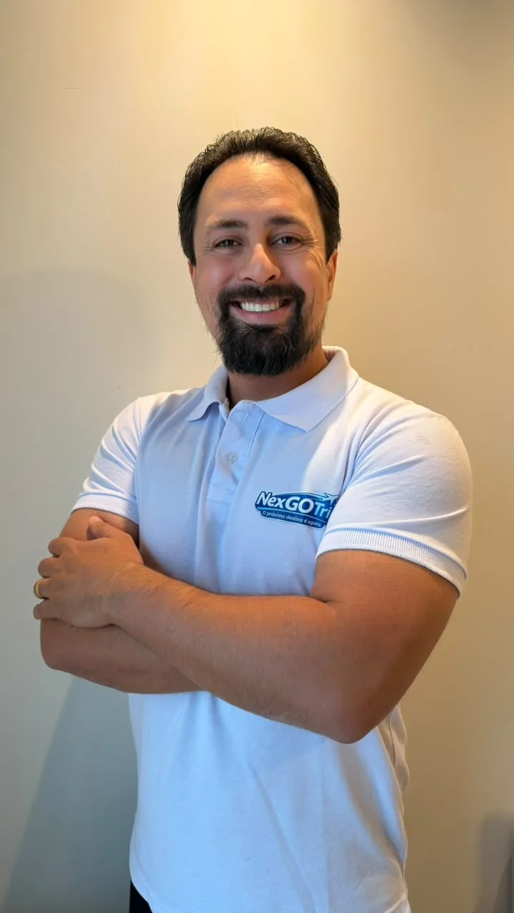 Darlam, da NexGo Trip, de camisa polo branca com a marca, sorrindo de braços cruzados